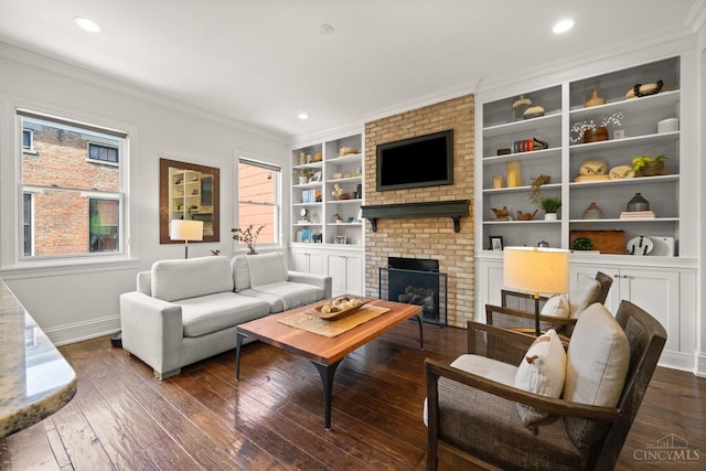 living area with dark wood-style floors, baseboards, crown molding, a brick fireplace, and built in shelves