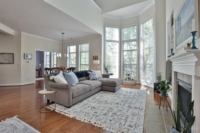 living area featuring ornamental molding, wood finished floors, a tile fireplace, baseboards, and a chandelier
