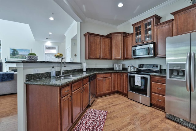 kitchen with appliances with stainless steel finishes, a sink, dark stone countertops, light wood finished floors, and crown molding