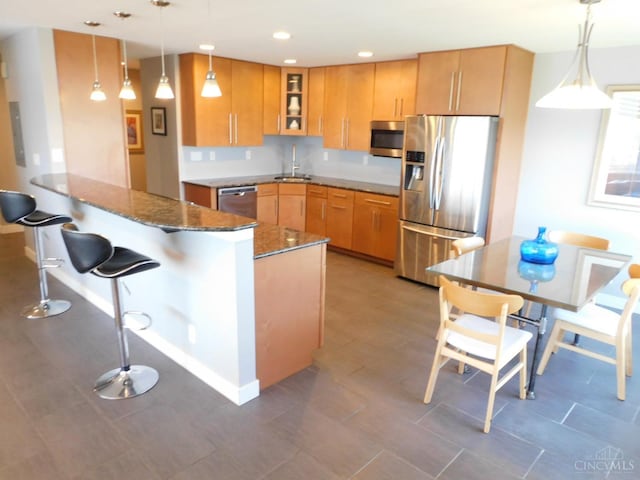 kitchen with stainless steel appliances, a peninsula, dark stone counters, glass insert cabinets, and pendant lighting