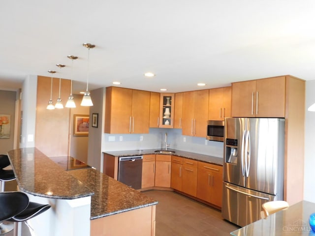 kitchen featuring appliances with stainless steel finishes, a peninsula, dark stone counters, glass insert cabinets, and a sink