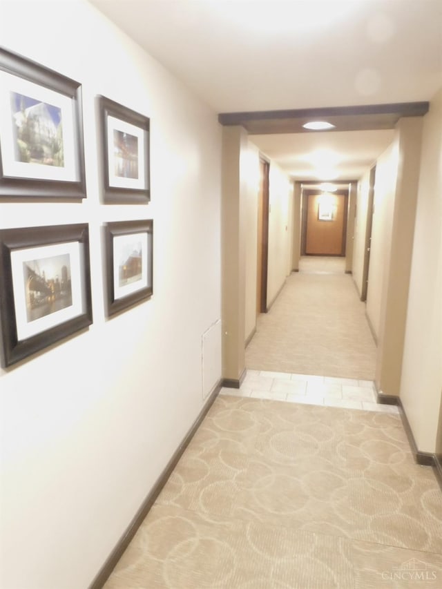 corridor featuring light colored carpet, baseboards, and light tile patterned floors