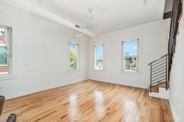 unfurnished living room featuring light wood-type flooring, healthy amount of natural light, stairs, and baseboards