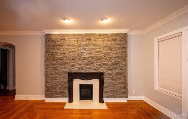 unfurnished living room featuring crown molding, arched walkways, a fireplace, wood finished floors, and baseboards