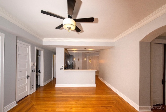 unfurnished living room featuring arched walkways, ceiling fan, crown molding, baseboards, and wood finished floors
