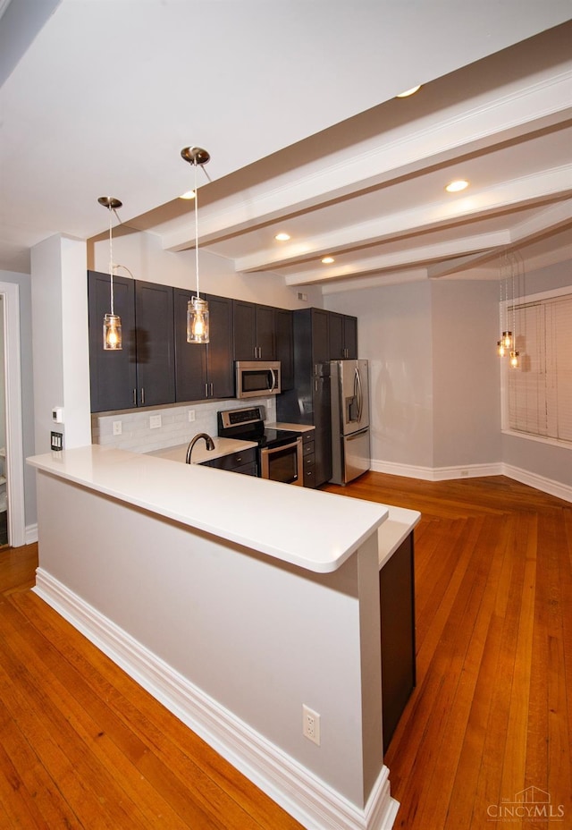 kitchen featuring stainless steel appliances, light countertops, a peninsula, decorative light fixtures, and hardwood / wood-style flooring