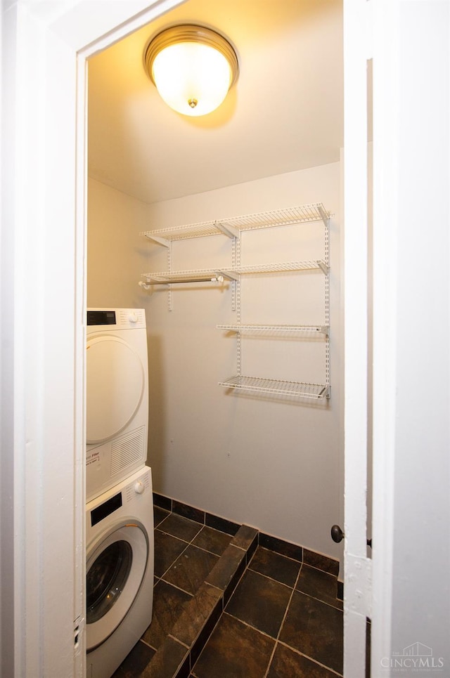 clothes washing area featuring stacked washer and clothes dryer and baseboards