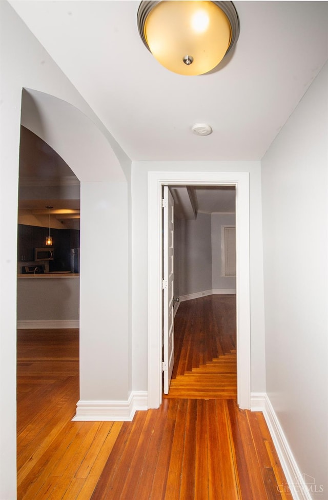 hall with wood-type flooring, arched walkways, and baseboards