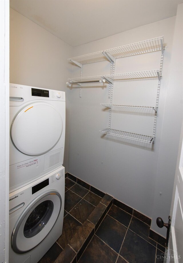 laundry room featuring estacked washer and dryer, baseboards, and dark tile patterned flooring