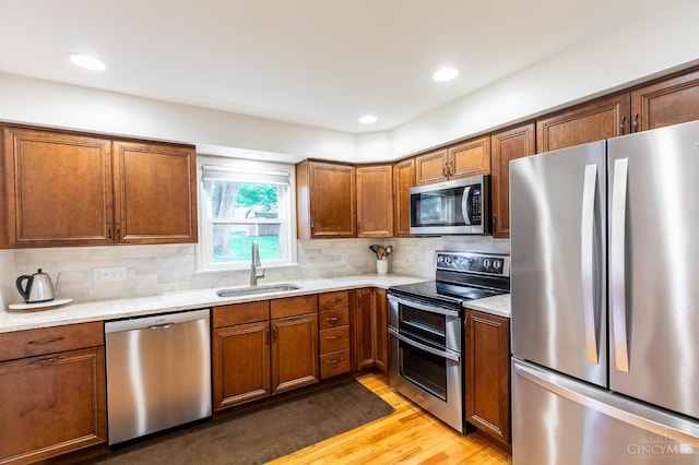 kitchen with stainless steel appliances, light wood finished floors, a sink, brown cabinets, and recessed lighting