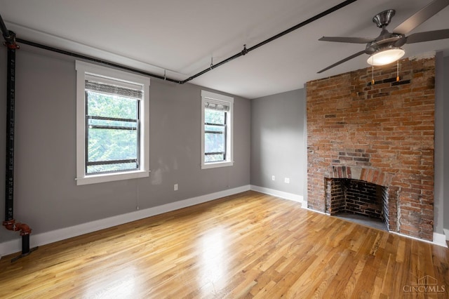 unfurnished living room with light wood-type flooring, a brick fireplace, a ceiling fan, and baseboards
