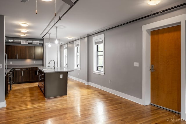 kitchen featuring light wood-type flooring, dark brown cabinetry, an island with sink, light countertops, and baseboards