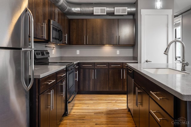 kitchen with stainless steel appliances, a sink, light wood-type flooring, and dark brown cabinets