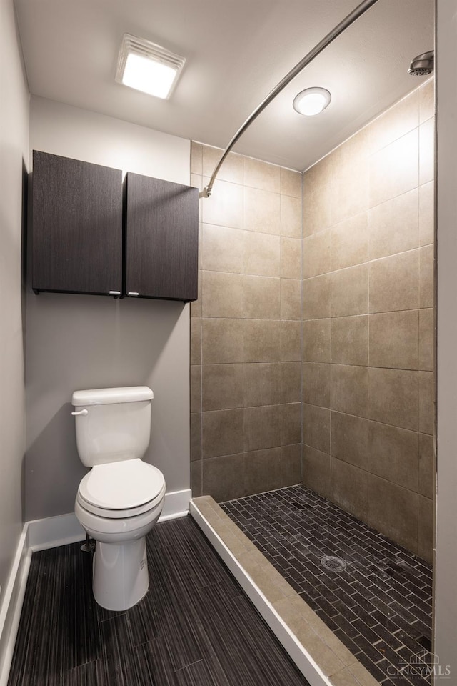 bathroom with toilet, baseboards, and a tile shower