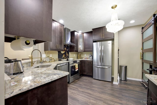 kitchen featuring stainless steel appliances, wall chimney range hood, a sink, dark brown cabinetry, and dark wood-style flooring