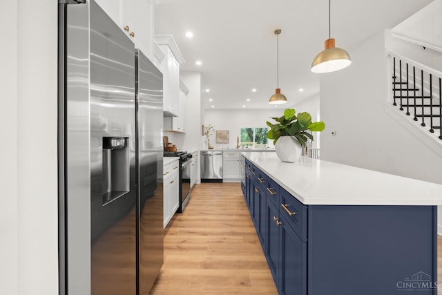 kitchen with appliances with stainless steel finishes, blue cabinets, light wood-type flooring, white cabinets, and light countertops