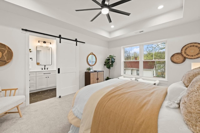 bedroom with a barn door, a sink, a tray ceiling, recessed lighting, and dark carpet