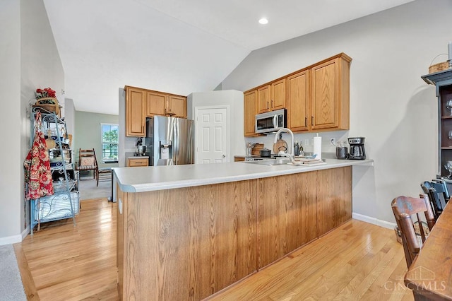 kitchen featuring stainless steel appliances, light wood-style floors, a peninsula, lofted ceiling, and light countertops