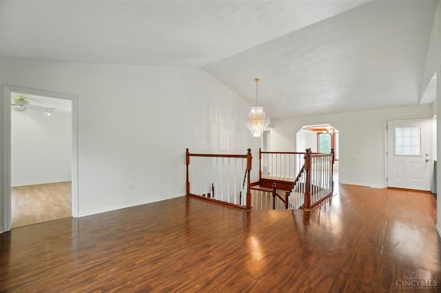 spare room featuring wood finished floors, lofted ceiling, arched walkways, and a chandelier