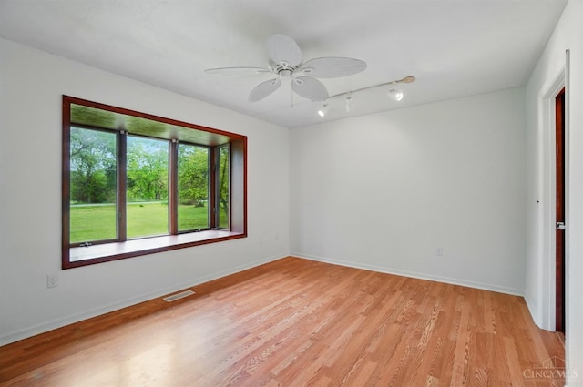 spare room with rail lighting, light wood-type flooring, a ceiling fan, and baseboards