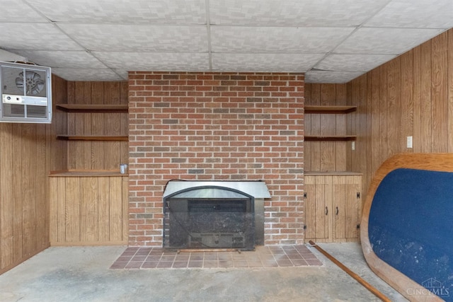 unfurnished living room with wood walls, a drop ceiling, and a fireplace with flush hearth