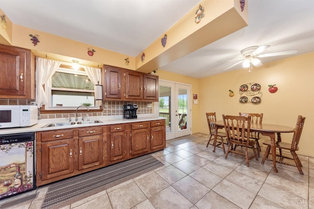 kitchen with a sink, white microwave, dishwasher, backsplash, and light countertops