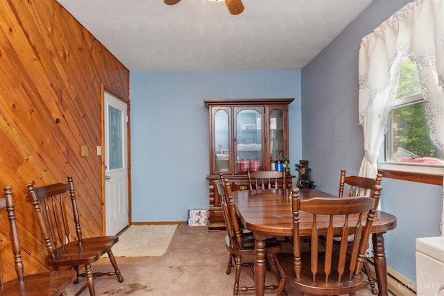 carpeted dining area with wood walls, a ceiling fan, and baseboard heating