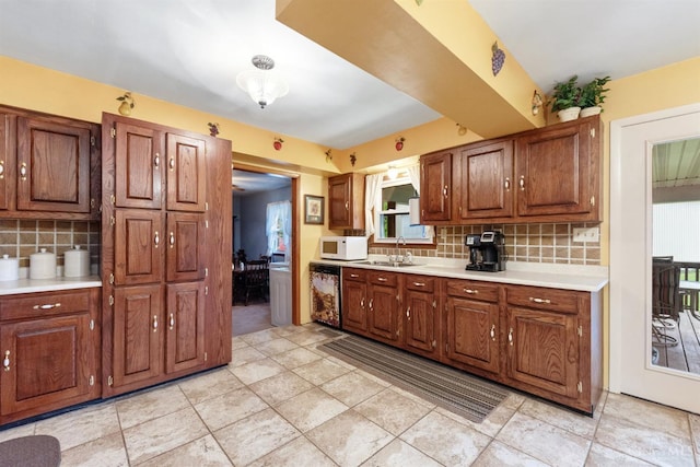 kitchen with white microwave, a sink, tasteful backsplash, light countertops, and dishwasher