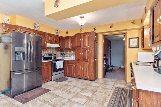 kitchen with appliances with stainless steel finishes, light countertops, under cabinet range hood, tasteful backsplash, and brown cabinets