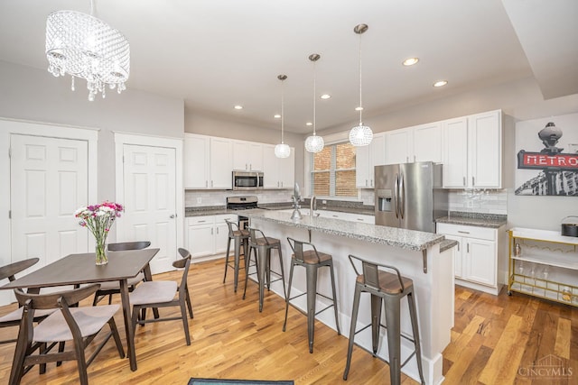 709 E Mcmillan St Unit 1, Cincinnati, OH 45206 - kitchen featuring appliances with stainless steel finishes, a kitchen bar, backsplash, white cabinetry, and light wood-type flooring