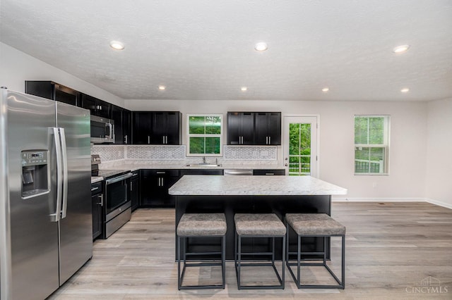 6482 Tralee Ln, Goshen Twp, OH 45122 - kitchen featuring appliances with stainless steel finishes, dark cabinetry, a breakfast bar, a center island, and decorative backsplash