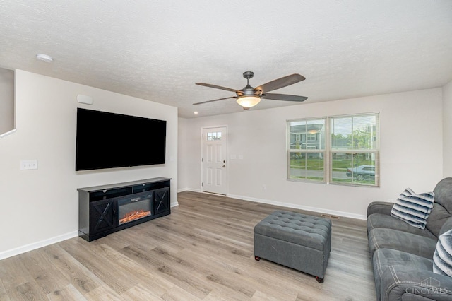 6482 Tralee Ln, Goshen Twp, OH 45122 - living room with light wood-type flooring, a ceiling fan, baseboards, a textured ceiling, and a glass covered fireplace