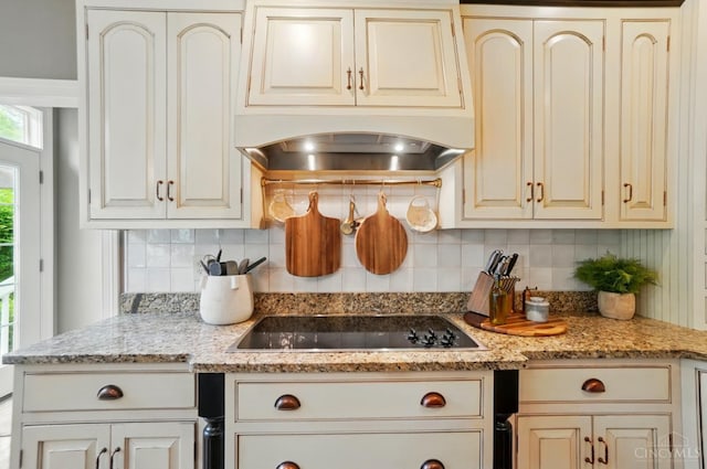 7757 Misty Meadows Ct, Harlan Twp, OH 45152 - kitchen with black electric cooktop, cream cabinetry, decorative backsplash, wall chimney exhaust hood, and light stone countertops