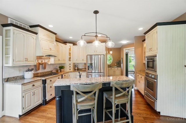 7757 Misty Meadows Ct, Harlan Twp, OH 45152 - kitchen featuring appliances with stainless steel finishes, a kitchen island, light stone counters, decorative backsplash, and light wood-style floors