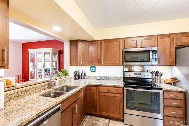 1627 Braintree Dr, Anderson Twp, OH 45255 - kitchen with stainless steel appliances, a sink, brown cabinets, light stone counters, and a textured ceiling