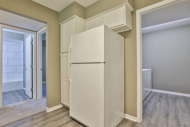 715 Castlegate Ln Unit 102, Springfield Twp, OH 45231 - kitchen featuring freestanding refrigerator, light wood-style flooring, white cabinets, baseboards, and separate washer and dryer