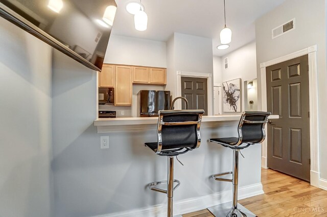 2110 Fulton Ave Unit 3, Cincinnati, OH 45206 - kitchen featuring black microwave, light brown cabinetry, a kitchen bar, light wood-style flooring, and freestanding refrigerator