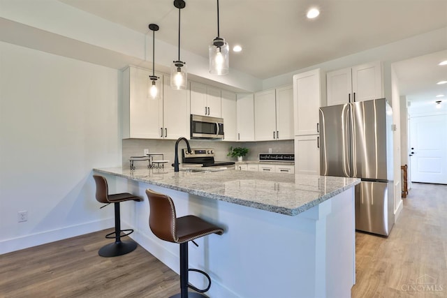 2351 Concord St, Cincinnati, OH 45206 - kitchen with stainless steel appliances, a peninsula, a breakfast bar area, white cabinets, and light stone counters