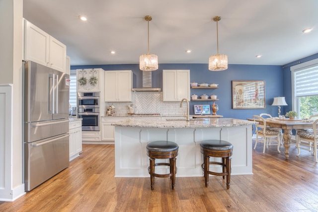 2645 Autumn Harvest Dr, Deerfield Twp, OH 45140 - kitchen featuring appliances with stainless steel finishes, wall chimney range hood, white cabinets, light wood finished floors, and backsplash