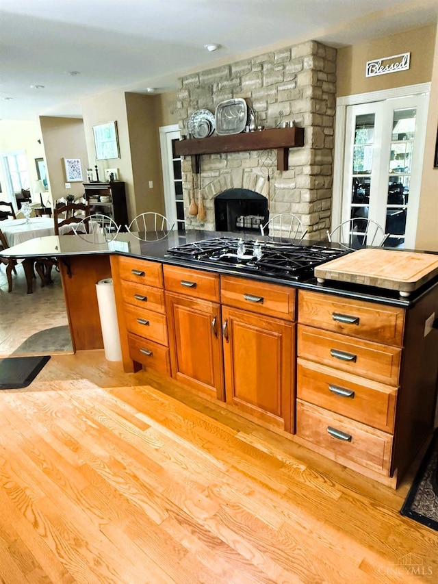 8030 Deershadow Ln, Montgomery, OH 45242 - kitchen with black gas stovetop, open shelves, a stone fireplace, light wood-type flooring, and brown cabinets