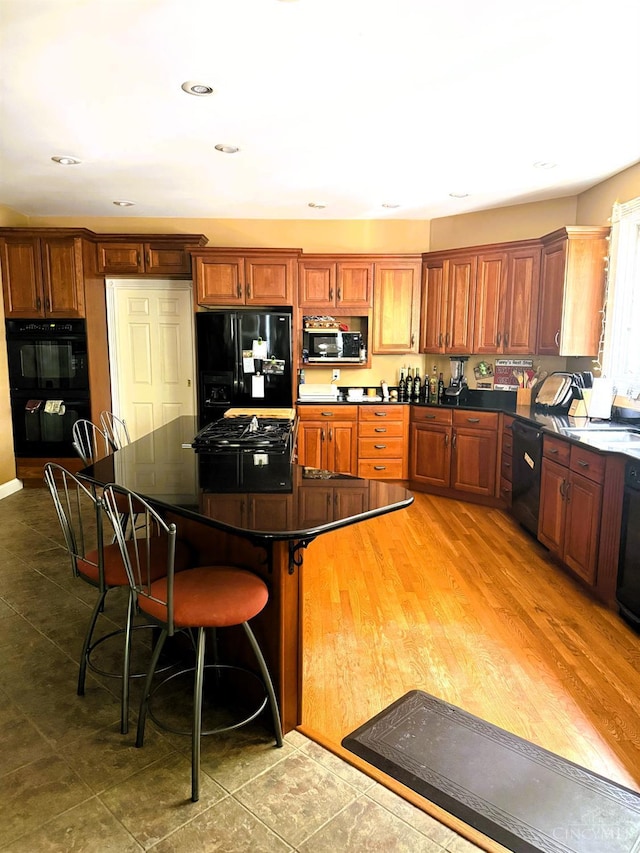 8030 Deershadow Ln, Montgomery, OH 45242 - kitchen with black appliances, dark countertops, a breakfast bar area, brown cabinetry, and a kitchen island