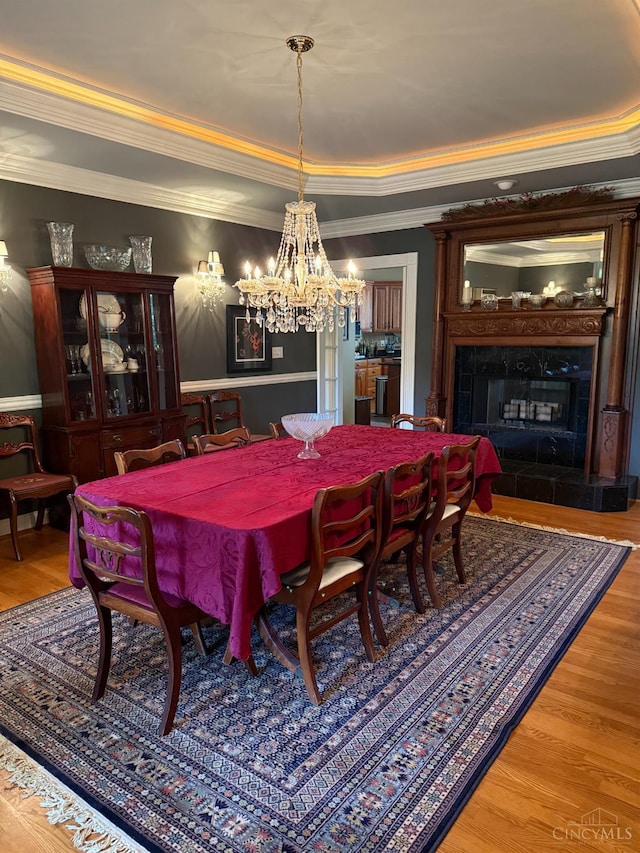8030 Deershadow Ln, Montgomery, OH 45242 - dining space featuring a premium fireplace, crown molding, a chandelier, wood finished floors, and a tray ceiling