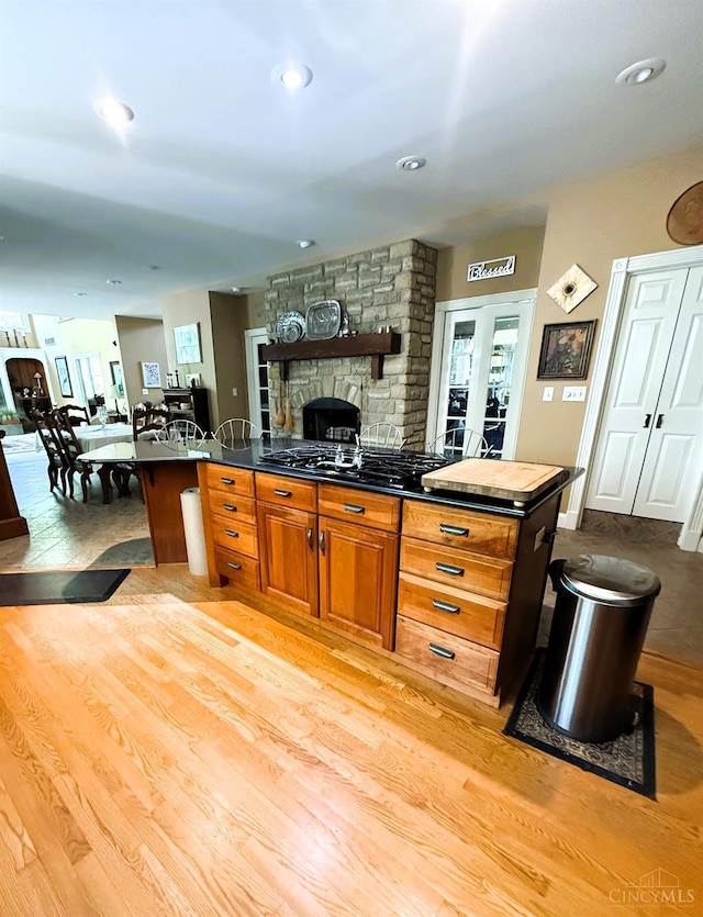 8030 Deershadow Ln, Montgomery, OH 45242 - kitchen featuring black gas cooktop, light wood-style flooring, a fireplace, brown cabinets, and a breakfast bar area