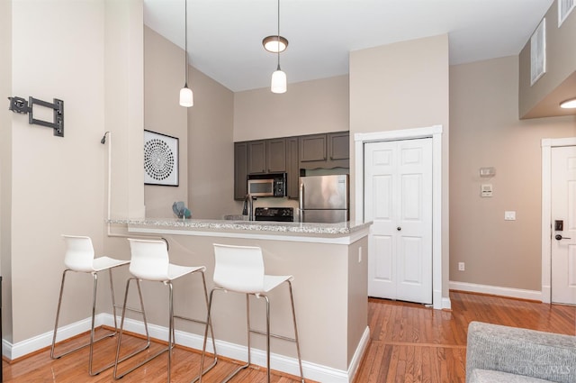2110 Fulton Ave Unit D1, Cincinnati, OH 45206 - kitchen featuring appliances with stainless steel finishes, a breakfast bar area, light wood-style flooring, a peninsula, and decorative light fixtures