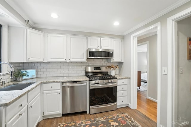 3862 Settle Rd, Mariemont, OH 45227 - kitchen with appliances with stainless steel finishes, wood finished floors, white cabinetry, decorative backsplash, and crown molding