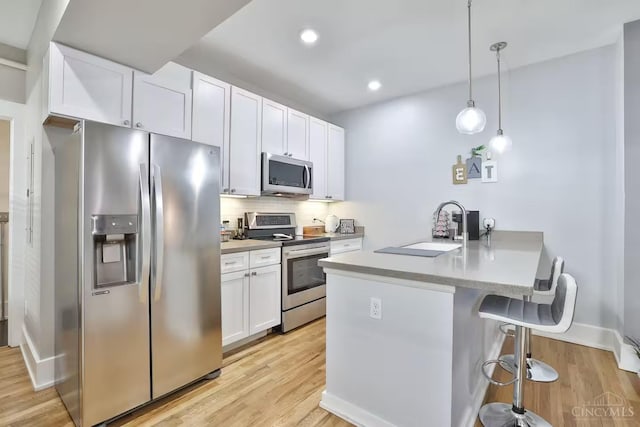 1407 Vine St Unit 303, Cincinnati, OH 45202 - kitchen featuring appliances with stainless steel finishes, a peninsula, a kitchen breakfast bar, light wood-style floors, and white cabinetry