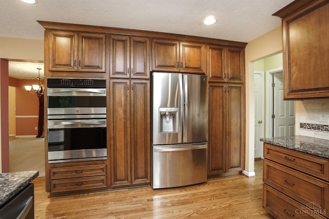 3779 Windyhollow Way, Mason, OH 45040 - kitchen with appliances with stainless steel finishes, light wood-type flooring, dark stone counters, tasteful backsplash, and brown cabinetry