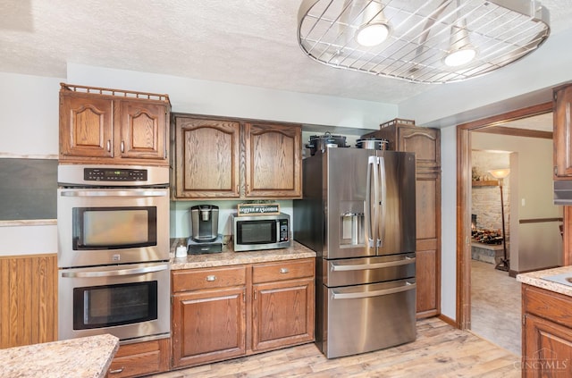 501 Tara Oaks Dr, Middletown, OH 45042 - kitchen featuring appliances with stainless steel finishes, light wood-style floors, brown cabinetry, and light stone counters