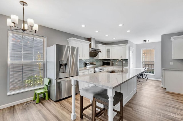 711 Van Roberts Pl, Wyoming, OH 45215 - kitchen with appliances with stainless steel finishes, wall chimney range hood, white cabinets, tasteful backsplash, and light wood finished floors