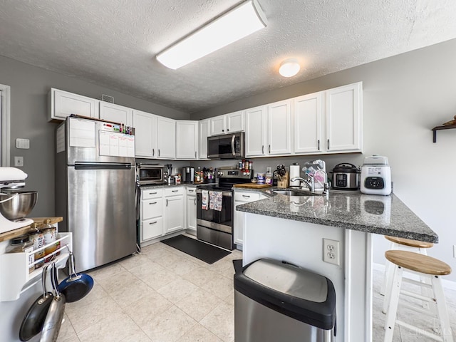 3649 Pebble Creek Ct, Mason, OH 45040 - kitchen featuring appliances with stainless steel finishes, a peninsula, white cabinetry, a textured ceiling, and dark stone countertops